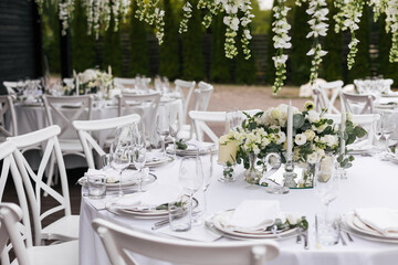 Served wedding table with decorative fresh white flowers and candles. Celebration details. Hanging flower beds and light bulbs Wedding decoration and decor, floristic concept