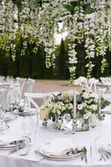 Served wedding table with decorative fresh white flowers and candles. Celebration details. Hanging flower beds and light bulbs Wedding decoration and decor, floristic concept