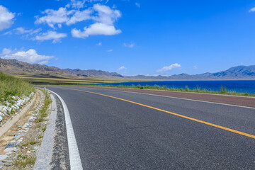 Asphalt road and lake with mountain natural scenery in Xinjiang, China.