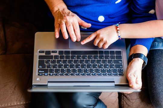 Crop mature person and child browsing computer on sofa
