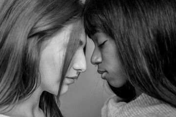 Couple of young lesbian women of different ethnicities head to head while looking down - Caucasian woman and African american girlfriend - Lgbtq and gay couple rights concept - Black and white editing