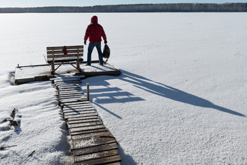 Frosty winter day. Ice on a river or lake. Tourist, traveler. Wooden bridge for fishing. Backpack in hand.