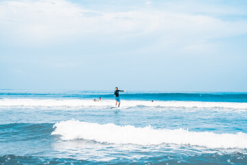 Fototapeta premium Surfing. A surfer on the waves in the ocean off the coast of Asia on the island of Bali in Indonesia. Sports and extreme. Beauty and health. Fashion and beach style.