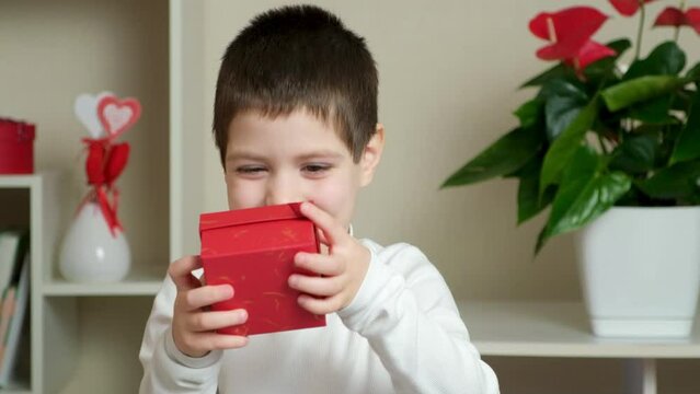 A cute 5-year-old boy gives a red box with a gift. Mother's Day, Father's Day or Valentine's Day