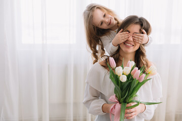 Happy mother's day concept. Child daughter congratulates mom and gives her flowers tulips. Mum and girl smiling and hugging. Family holiday and togetherness.