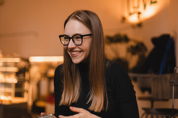 Charming woman with beautiful smile reading good news on mobile phone during rest in coffee shop, happy Caucasian female watching her photos on cell telephone while relaxing in cafe during free time.