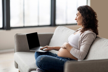 Fototapeta na wymiar Smiling Pregnant Woman Using Laptop With Blank Black Screen At Home