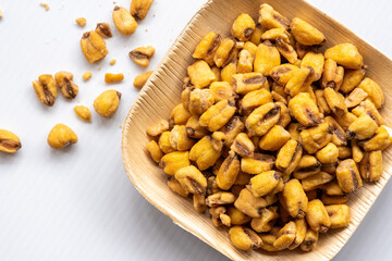 Roasted crunchy corn, seasoned with salt, a healthy snack, is served in a biodegradable palm leaf tray on a white background. Healthy eating. Overhead viiew.