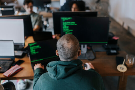 Rear view of male programmer coding on computer at creative office
