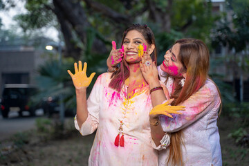 Two young girls sisters friends family celebrating enjoying holi festival of colors colours outdoor in a park