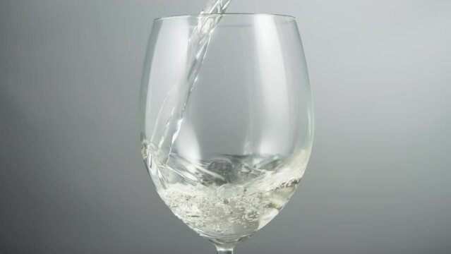 Close up of pouring white wine in a wineglass on a grey background. Slow motion.