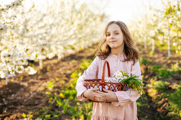 Beautiful caucasian blonde girl in a pink dress with a basket in the garden of flowering trees in spring. 