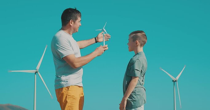 Happy father and son on looking at wind energy turbine sat wind farm site, alternative energy, wind farm and happy time with your family.

