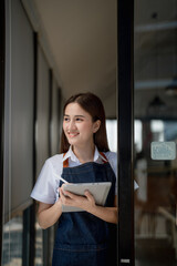 open a small business Portrait of happy Asian woman in apron holding tablet in front of cafe.