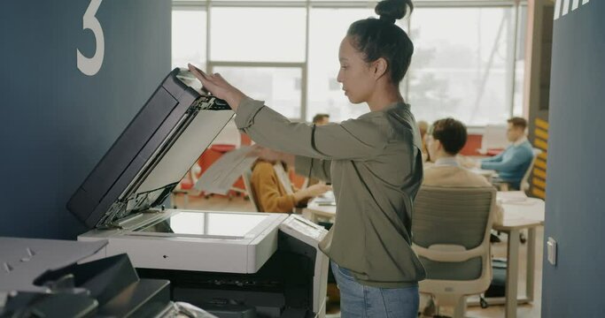 Young mixed race businesswoman is using multifunctional copy machine in coworking space. Business activities and equipment concept.