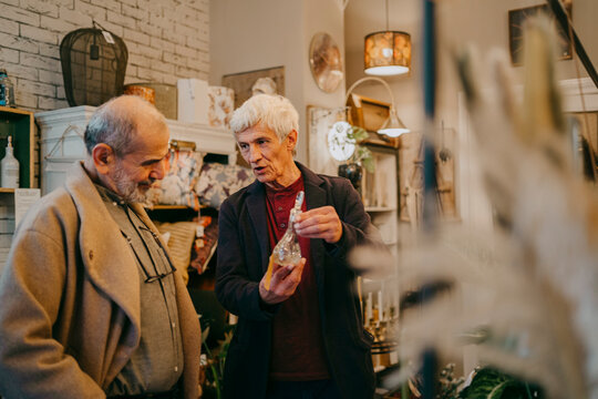 Senior male owner showing glass figurine to customer at home decor store