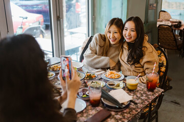 Woman photographing female friends sitting with food at restaurant