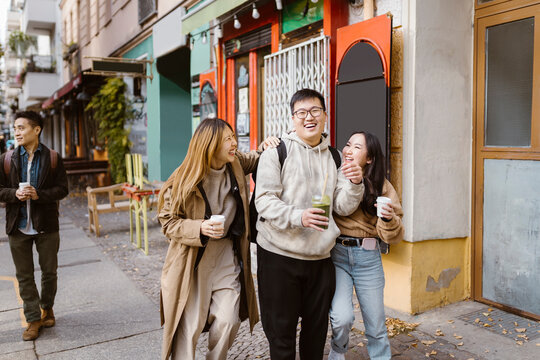 Cheerful male and female friends talking while walking on sidewalk