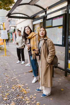 Female friends looking away while waiting at bus stop