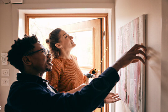 Couple assisting each other while hanging painting on wall near doorway at home