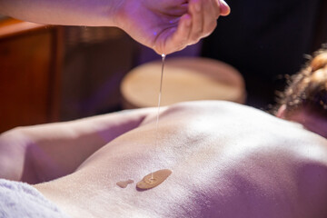 Detalhe do terapeuta derramando óleo nas costas de uma paciente que está deitada em uma maca.