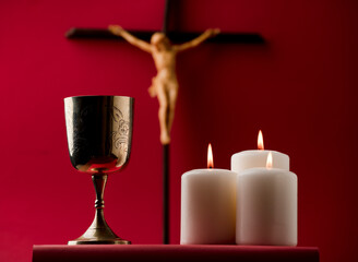 golden chalice with crucifix and burning candles red background