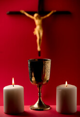 golden chalice with crucifix and burning candles red background