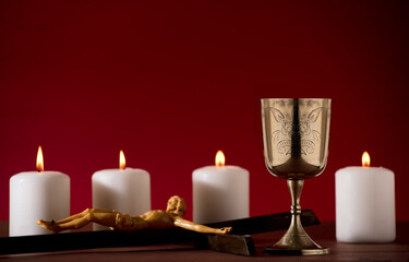 Fototapeta na wymiar golden chalice with crucifix and burning candles red background