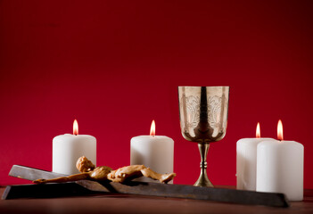 golden chalice with crucifix and burning candles red background