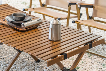 stainless steel kettle, chair,portable gas stove, bowl and vintage lanterns on outdoor wooden table in camping area - obrazy, fototapety, plakaty