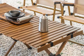 Fotobehang stainless steel kettle, chair,portable gas stove, bowl and vintage lanterns on outdoor wooden table in camping area © xiaoliangge