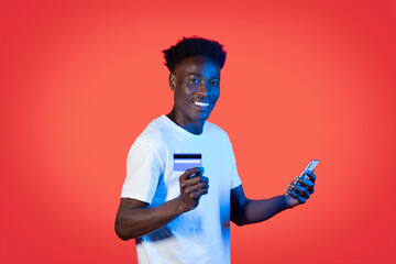 Cheerful black guy using smartphone and credit card, online banking