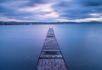 Long exposure photography of a woddden pier on the sea, the water is calm and silky the clouds are blurry because of movement