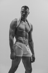 Black and white portrait of muscular male fashion model over grey studio background. Man posing shirtless. Masculinity. Concept of men's health, beauty, body and skin care, fitness.