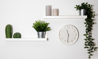 Pared blanca con estanterías blancas, plantas de decoración, velas y un reloj circular
