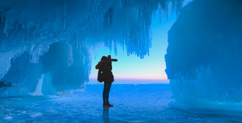 Silhouette of a lonely photographer girl taking a photo -   Inside the turquoise ice cave - ice cave winter frozen nature background landscape - Lake Baikal, Siberia, Eastern Russia
