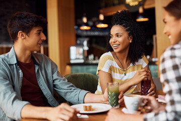 Young African American woman enjoys while talking to her friends in cafe.