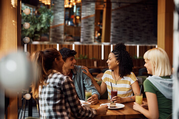 Multiracial group of happy friends talk while gathering in cafe.