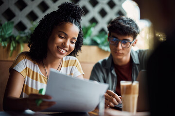 Happy black student and her friend preparing for upcoming exams in cafe.