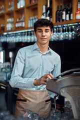 Young waiter preparing coffee and looking at camera.