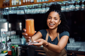 Happy African American waitress serving fruit juice and looking at camera.