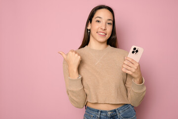 young brunette girl wearing casual sweater against pink wall using and texting with smartphone...