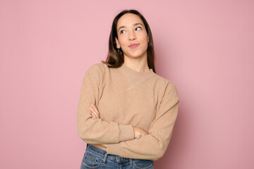 Fototapeta premium pretty young woman feeling happy, proud and hopeful, wondering or thinking, looking up to copy space with crossed arms