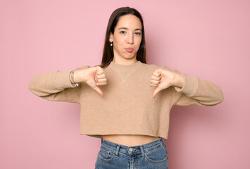 Young caucasian woman isolated on pink background showing thumb down with two hands