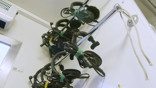 Headphones with wires and microphones for employees hang on metal pipe in SNG van. Devices hang against wall in storage room