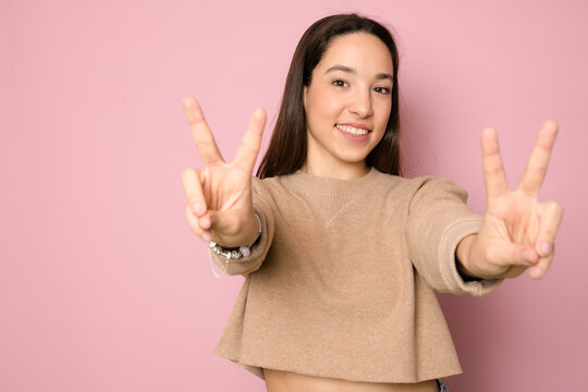 Picture of smiling emotional young lady isolated over pink background make peace gesture and looking camera.