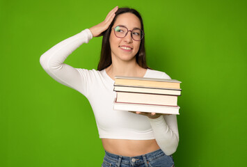 Happy girl holding in hands a pile of books isolated over green background.