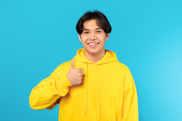 Happy Asian Teenager Guy Gesturing Thumbs Up On Blue Background