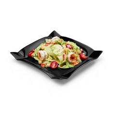 Caesar salad with shrimp on a black plate on a white background isolated
