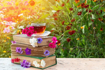 A cup of tea on stack of books with flowers, sunny summer day. Copy space